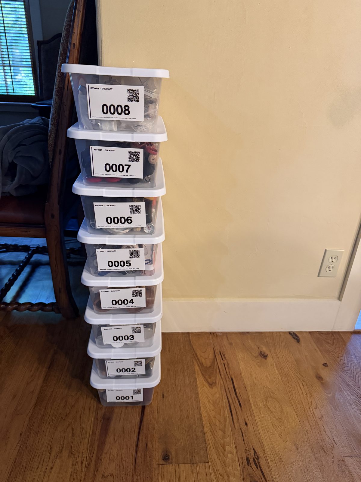 Eight clear storage tubs lined up on a wood table, each labeled with a large number (0001 to 0008) and a QR code.