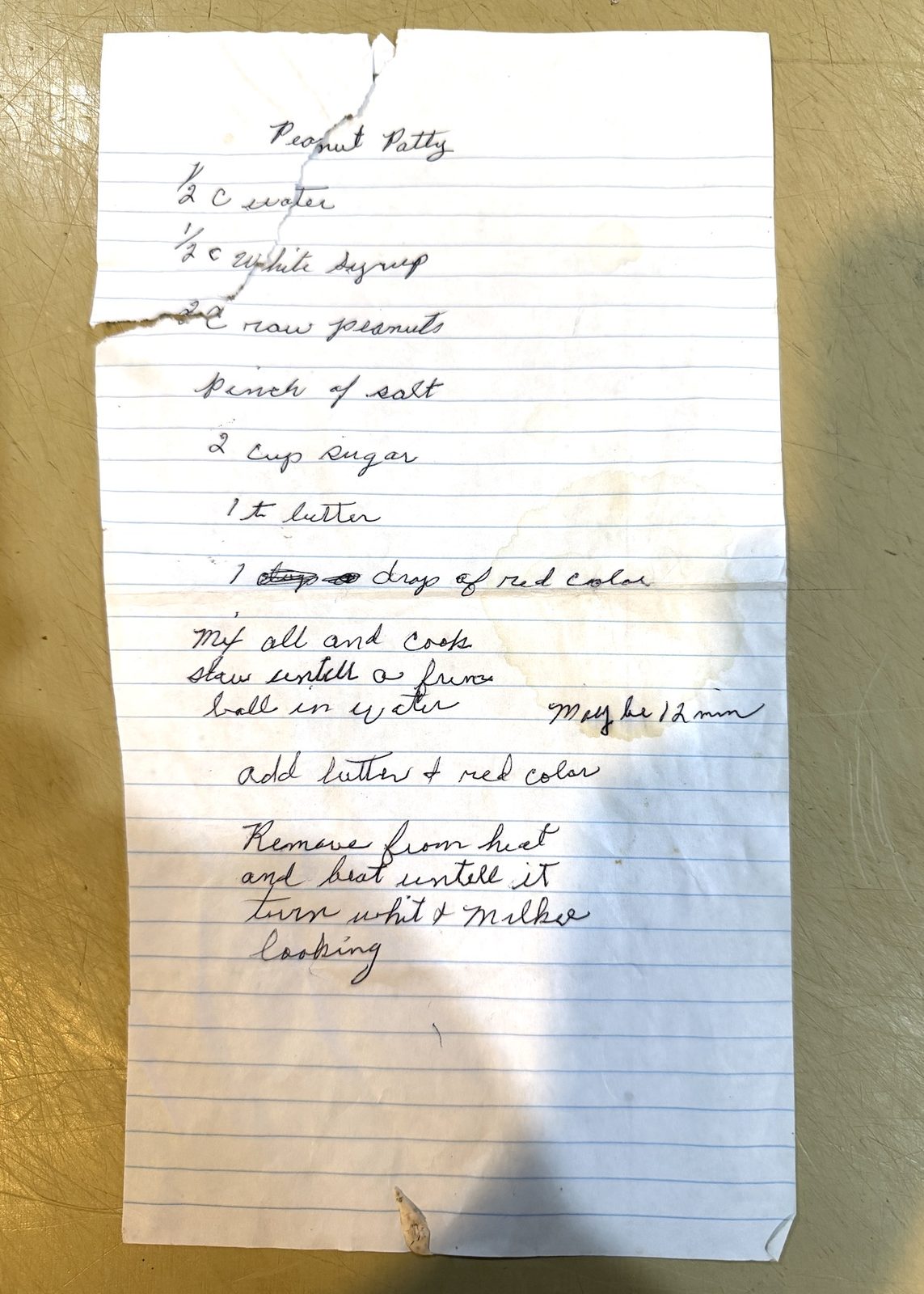 My mom's handwritten peanut patty recipe, in cursive ballpoint on a small sheet of notebook paper torn at the top, with a margin note reading 'Maybe 12 min.'